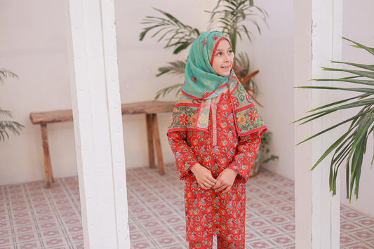 Person wearing a red and green patterned outfit with a matching headscarf in a room with plants.