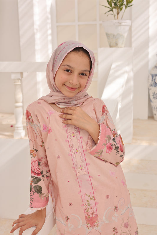 Young girl in a pink floral dress and hijab standing indoors with a neutral background