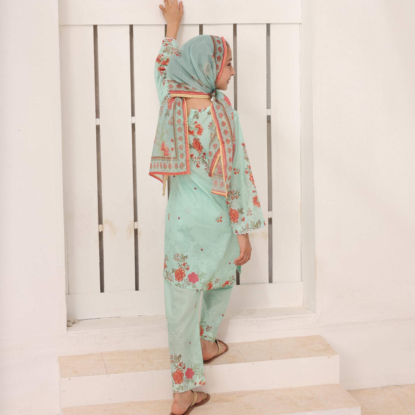 Person wearing a light blue dress with floral patterns leaning against a white wall.