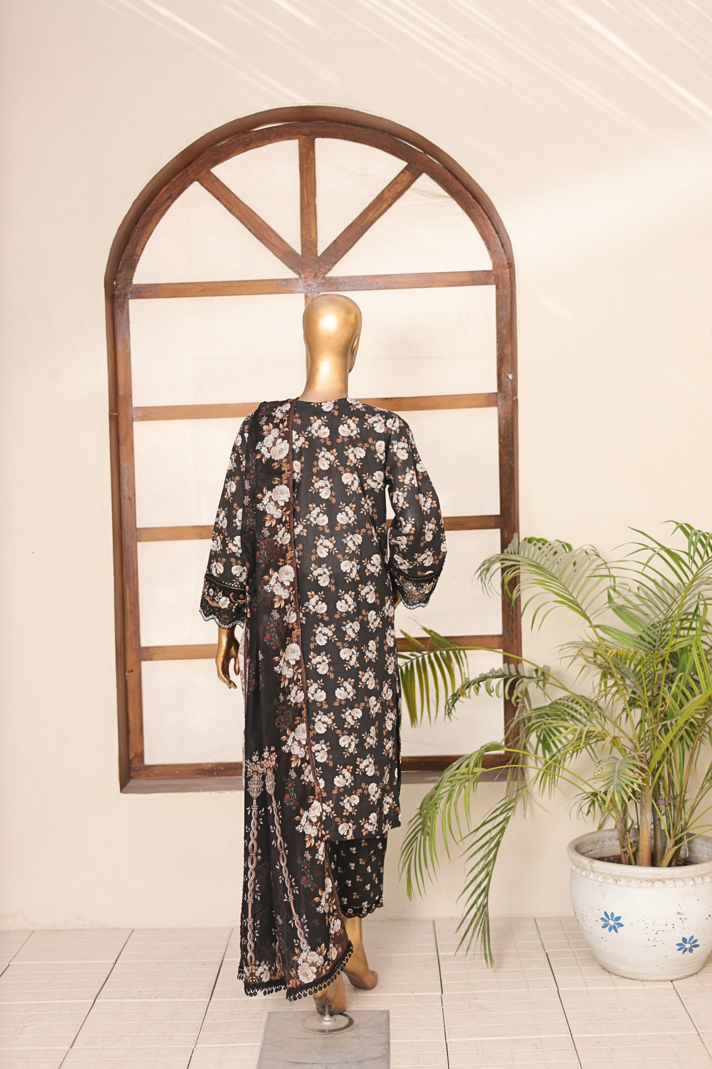 Mannequin wearing a black floral dress in front of a decorative mirror with a plant to the side.