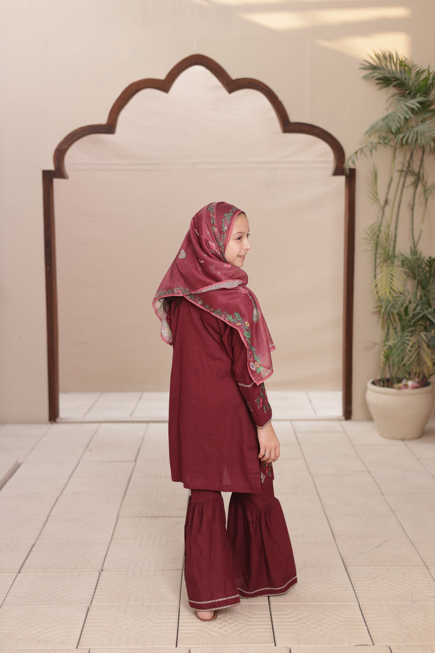 Woman in a burgundy outfit standing in front of a decorative mirror.