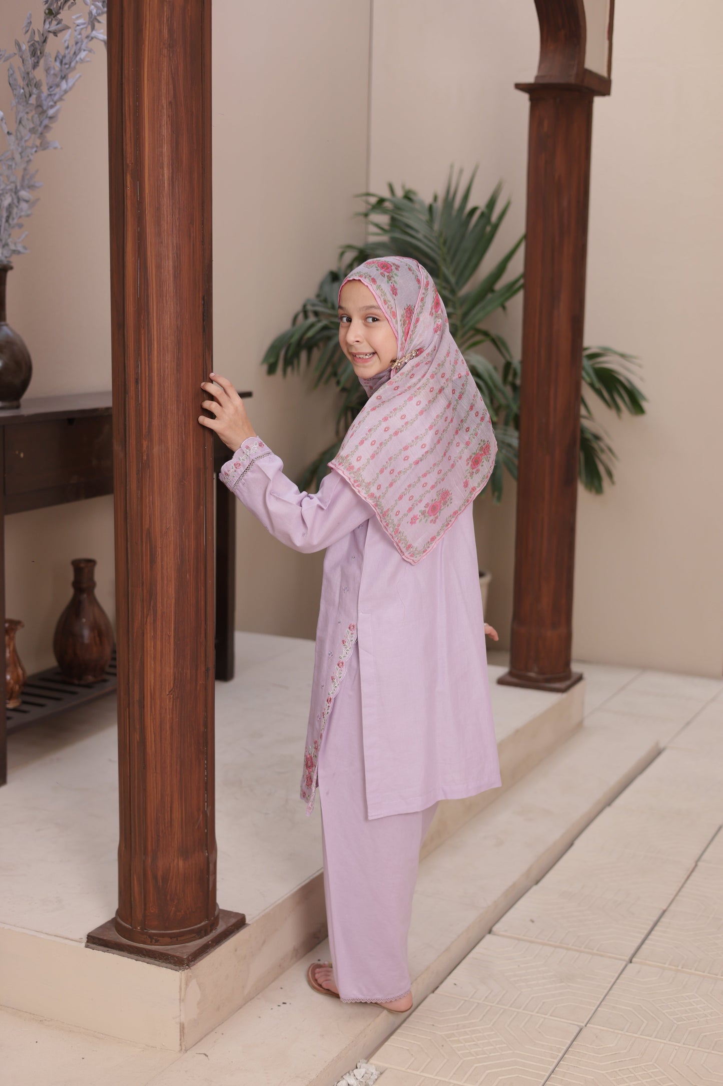Person in a light purple outfit with a floral headscarf standing on a staircase.