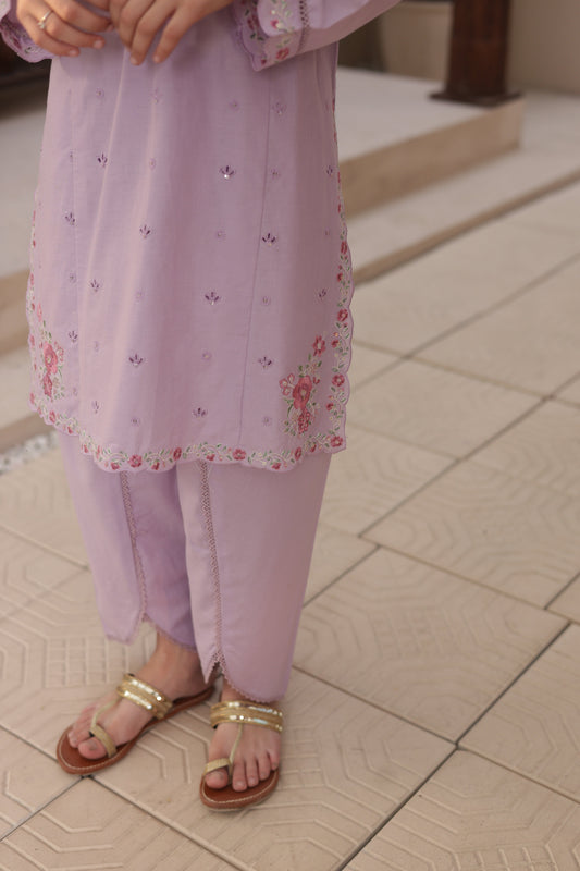 Person wearing a light purple dress with floral cuffs on a tiled floor.