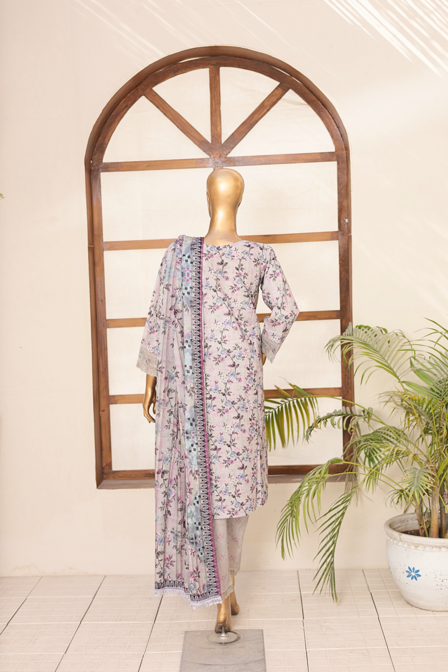 Mannequin wearing a floral dress with a matching scarf in front of a decorative window.