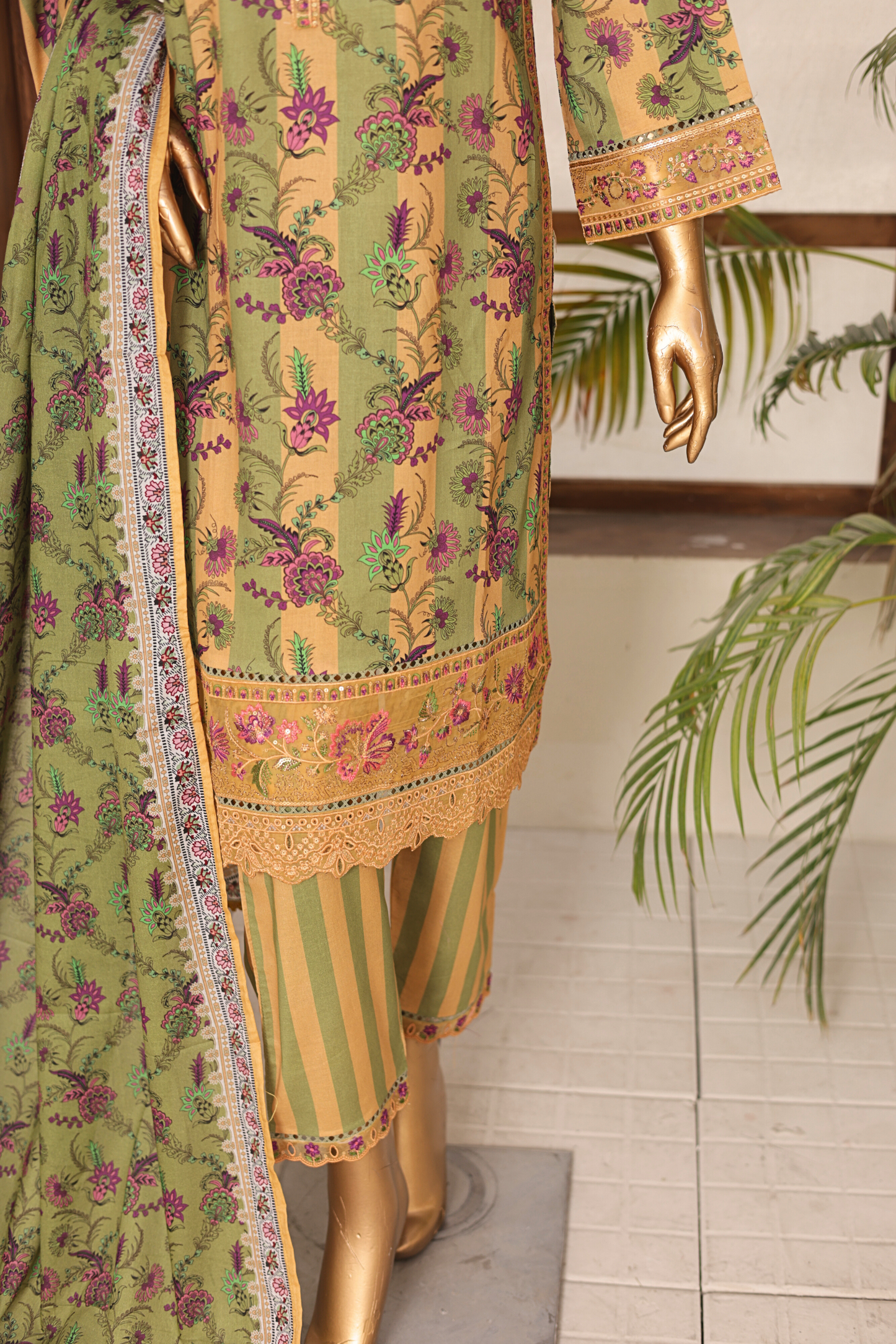 Traditional green and yellow embroidered outfit on a mannequin with a plant in the background