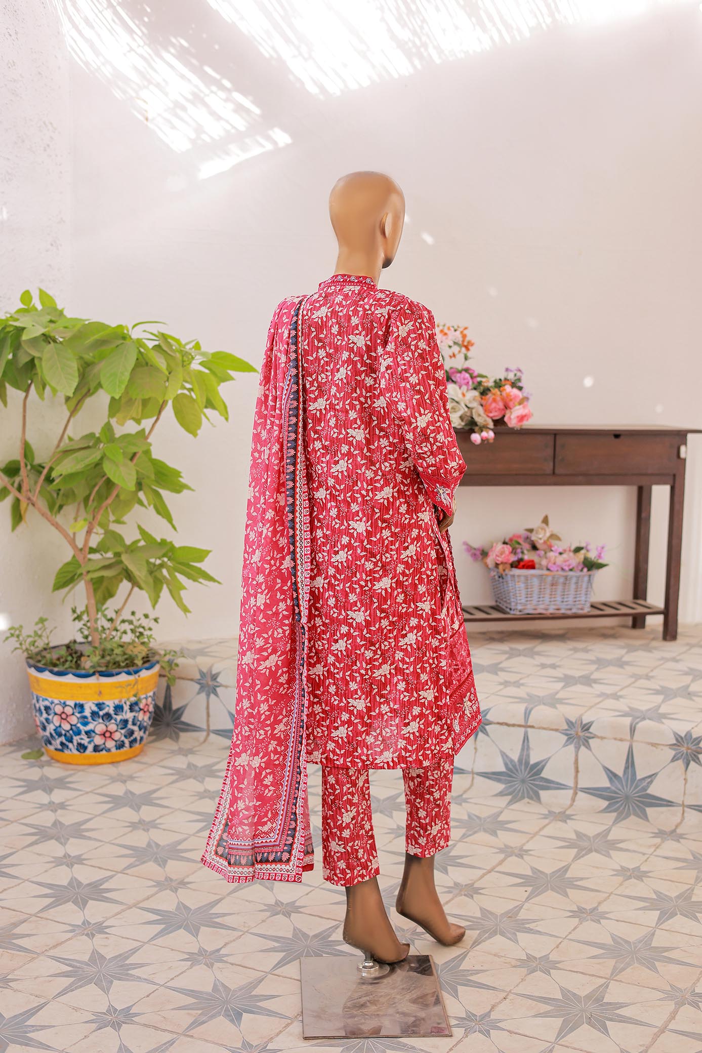 Mannequin wearing a red floral outfit with a matching dupatta in a room with decorative elements.