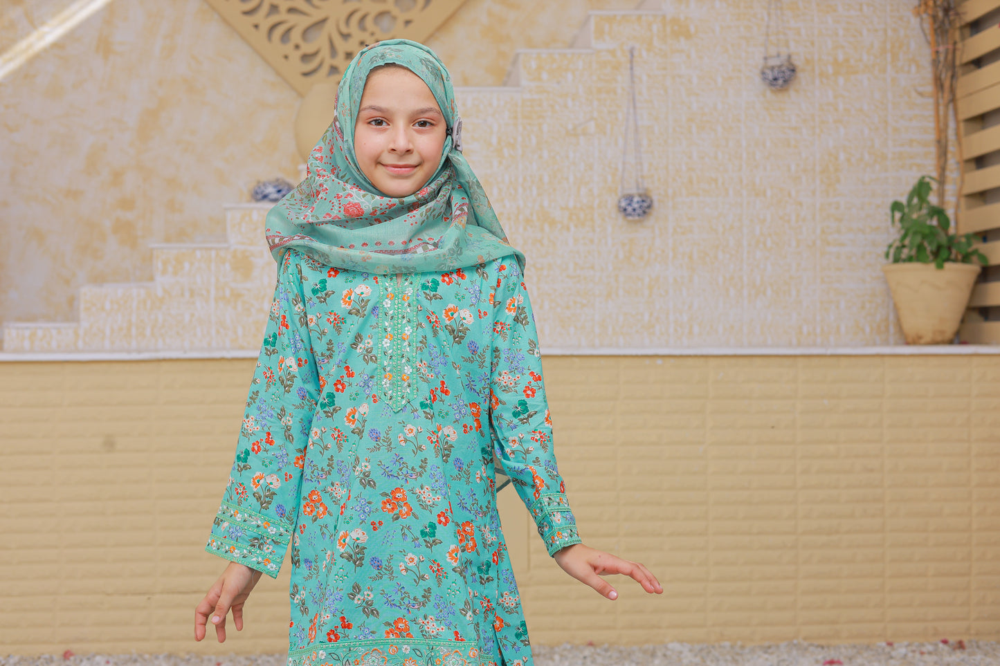 Young girl wearing a green floral dress and headscarf in a bathroom setting.