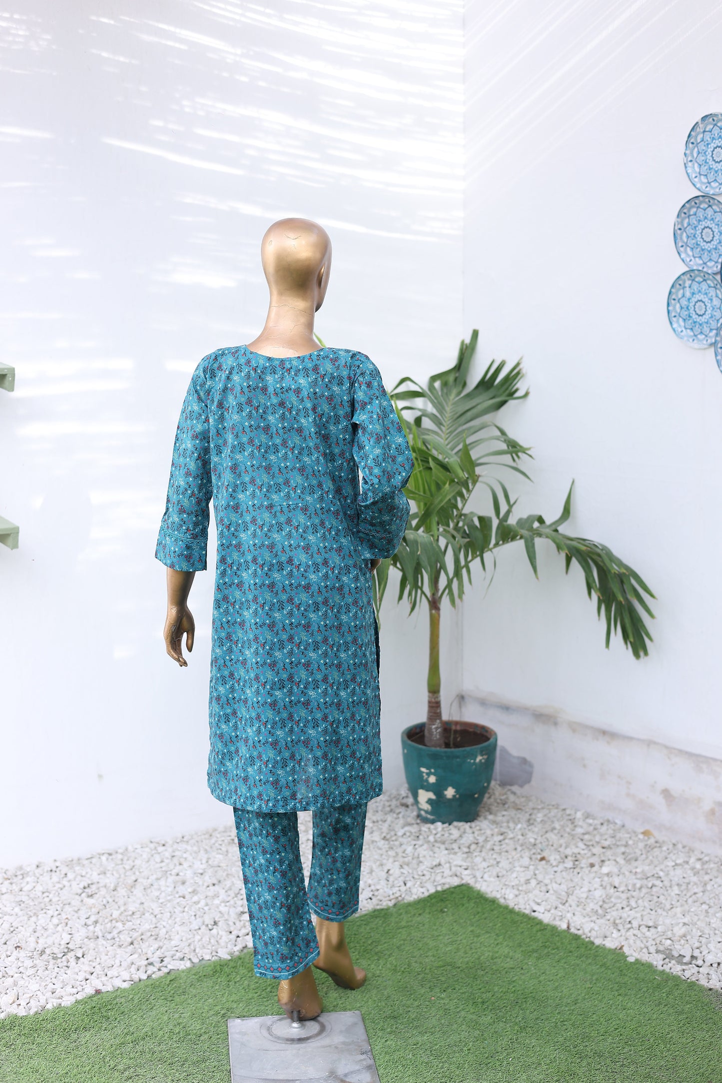 Mannequin wearing a blue patterned outfit with a potted plant on a white background