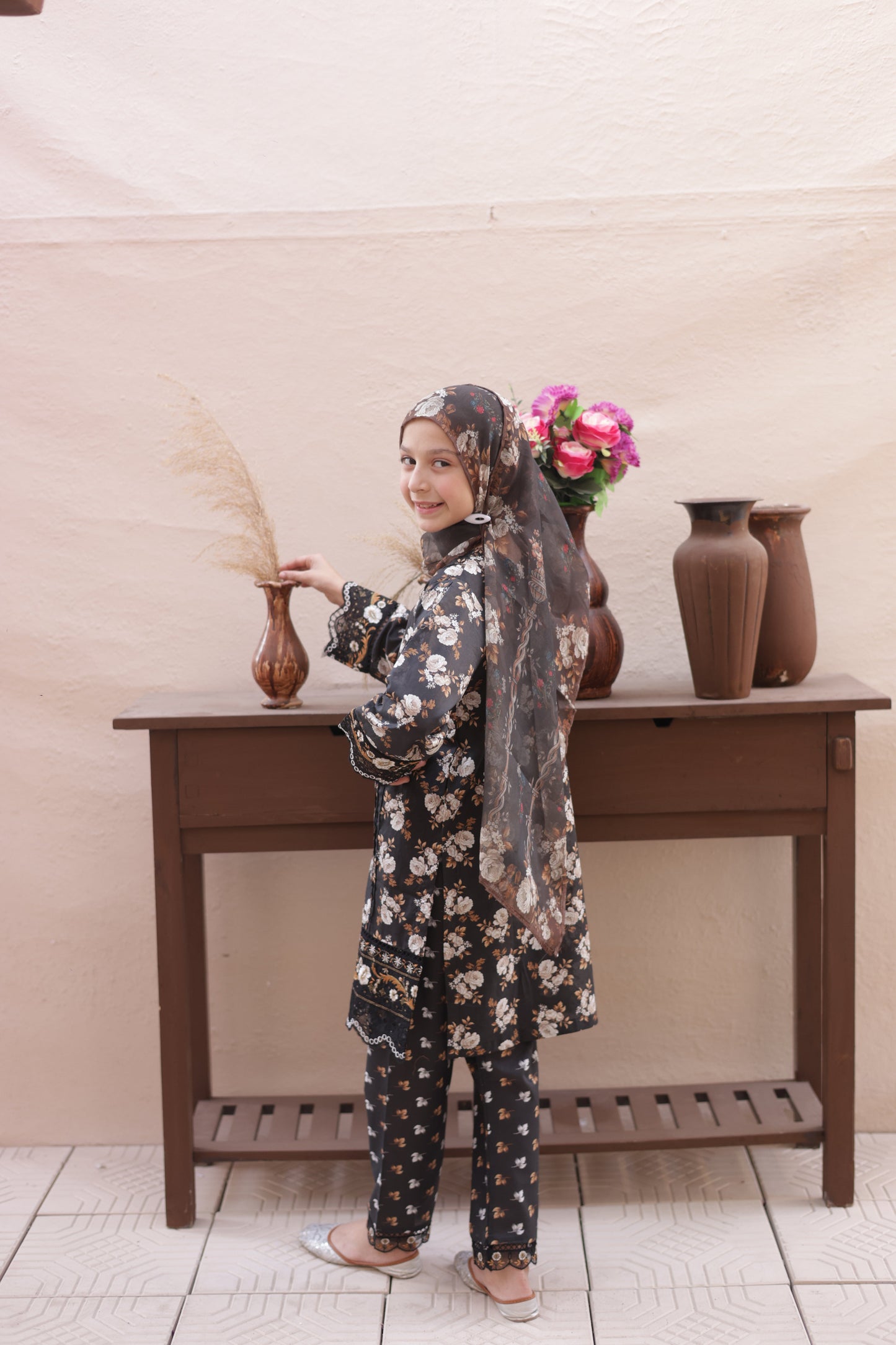 Person wearing a floral dress and polka dot pants standing next to a wooden stool.