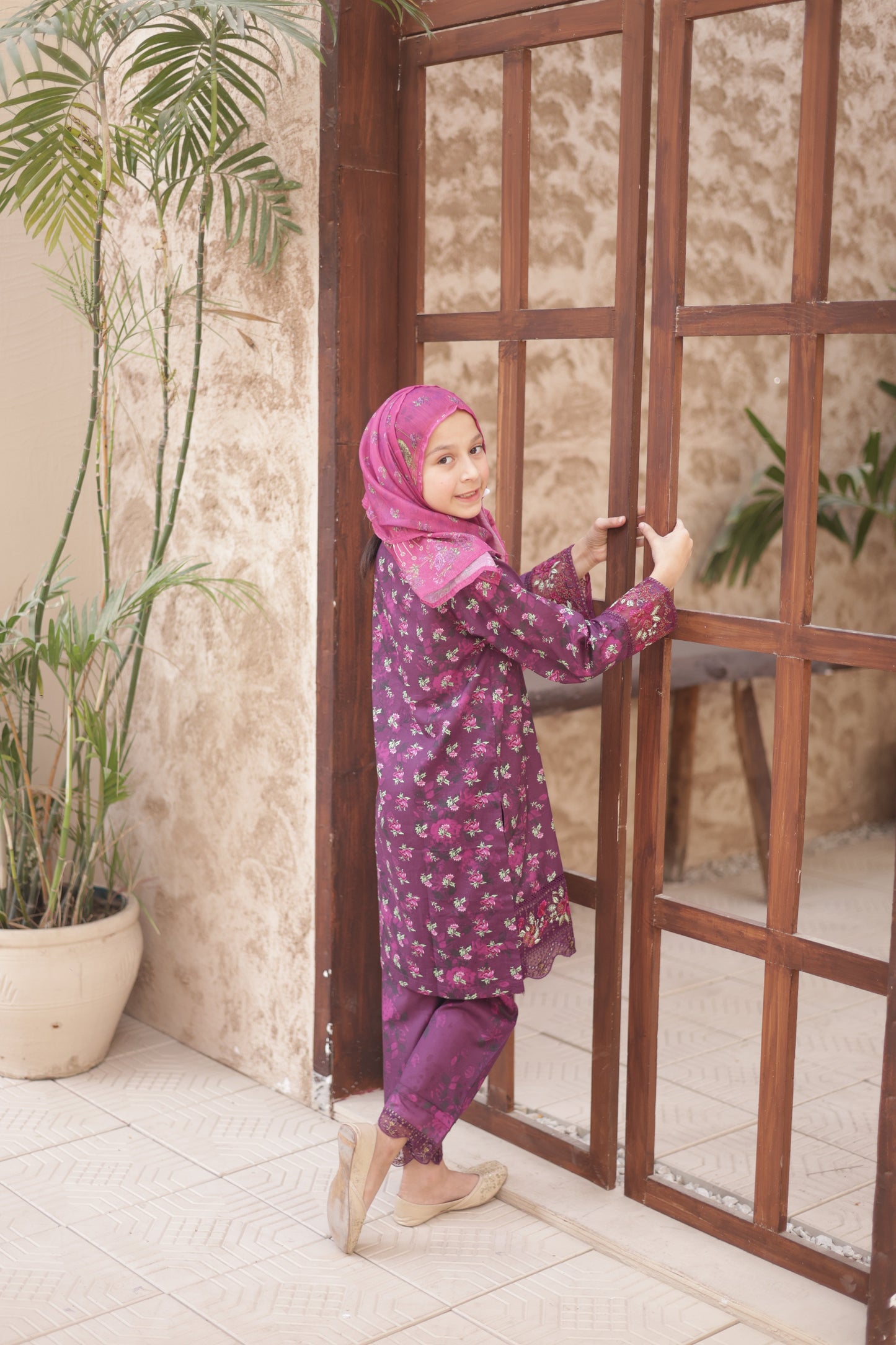 Person in a purple outfit with a pink hijab standing on a wooden staircase.