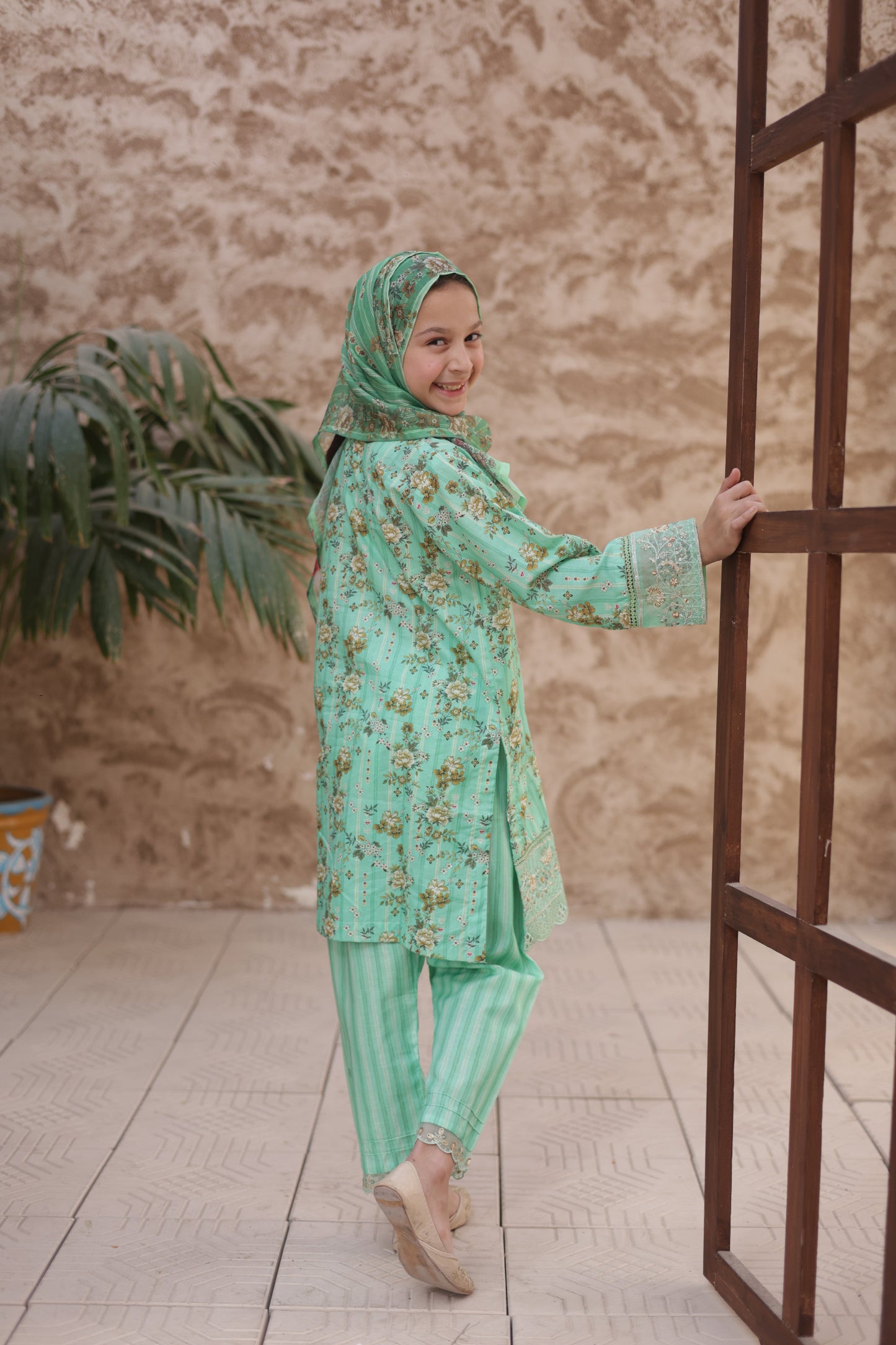 Person in a green traditional outfit standing on a wooden structure with a neutral background