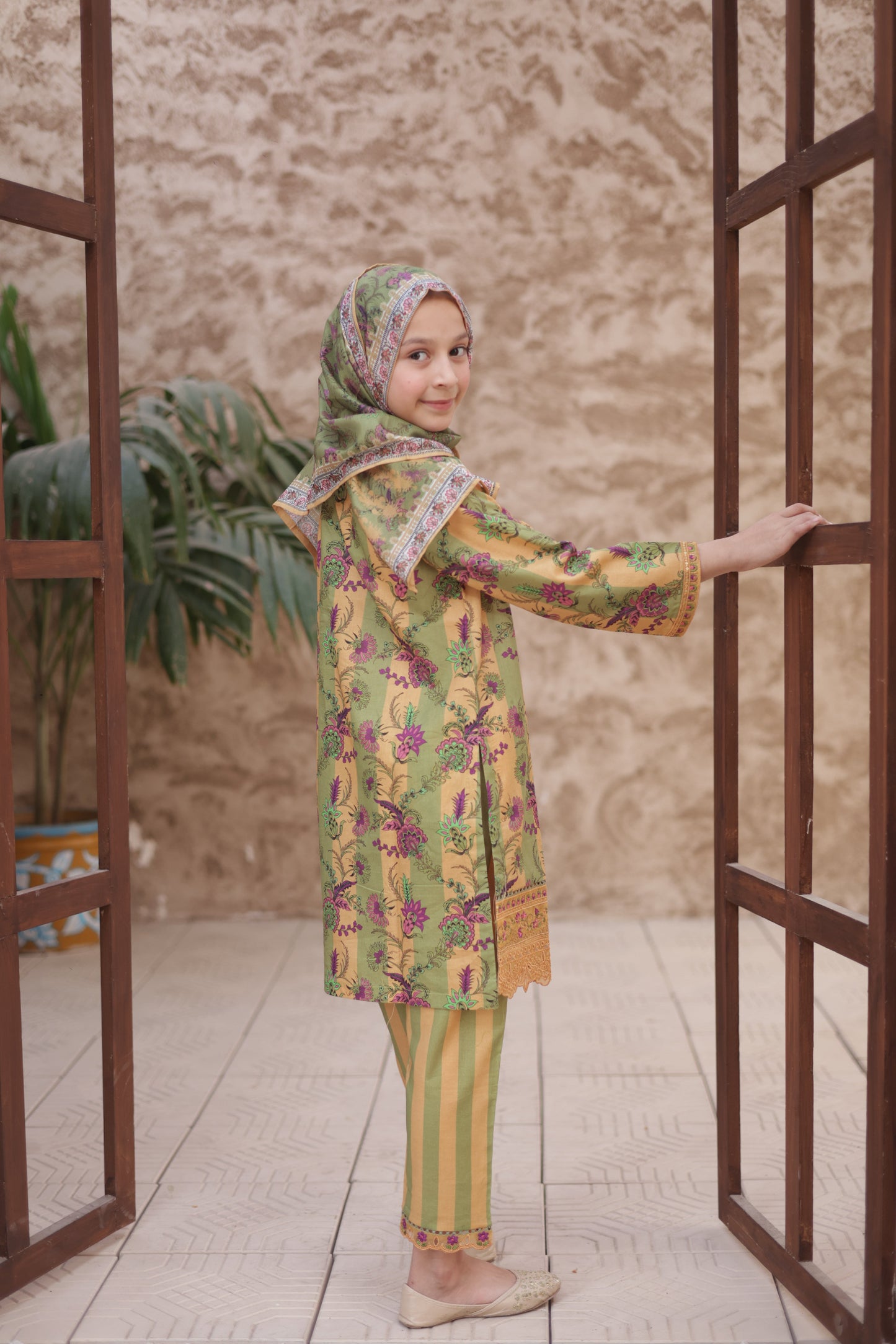 Child in a colorful outfit standing on a wooden floor with a mirror reflection.