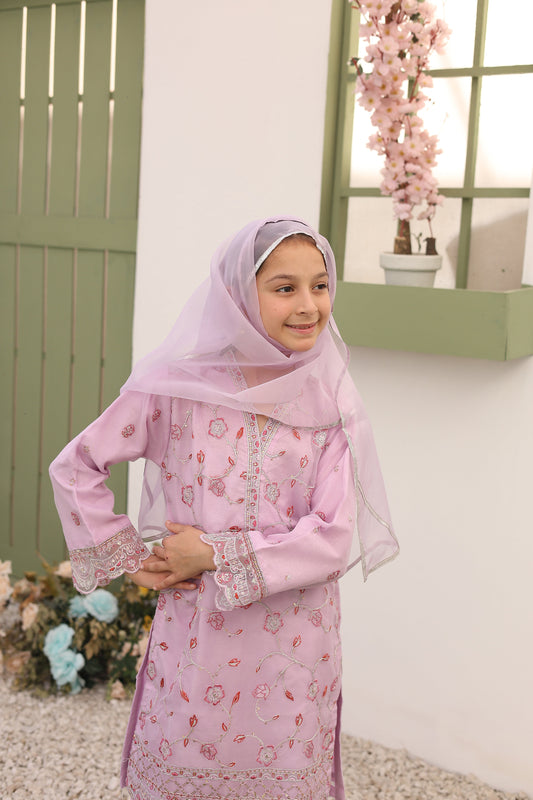 Young girl in a pink traditional outfit with a hijab, sitting on a white surface.