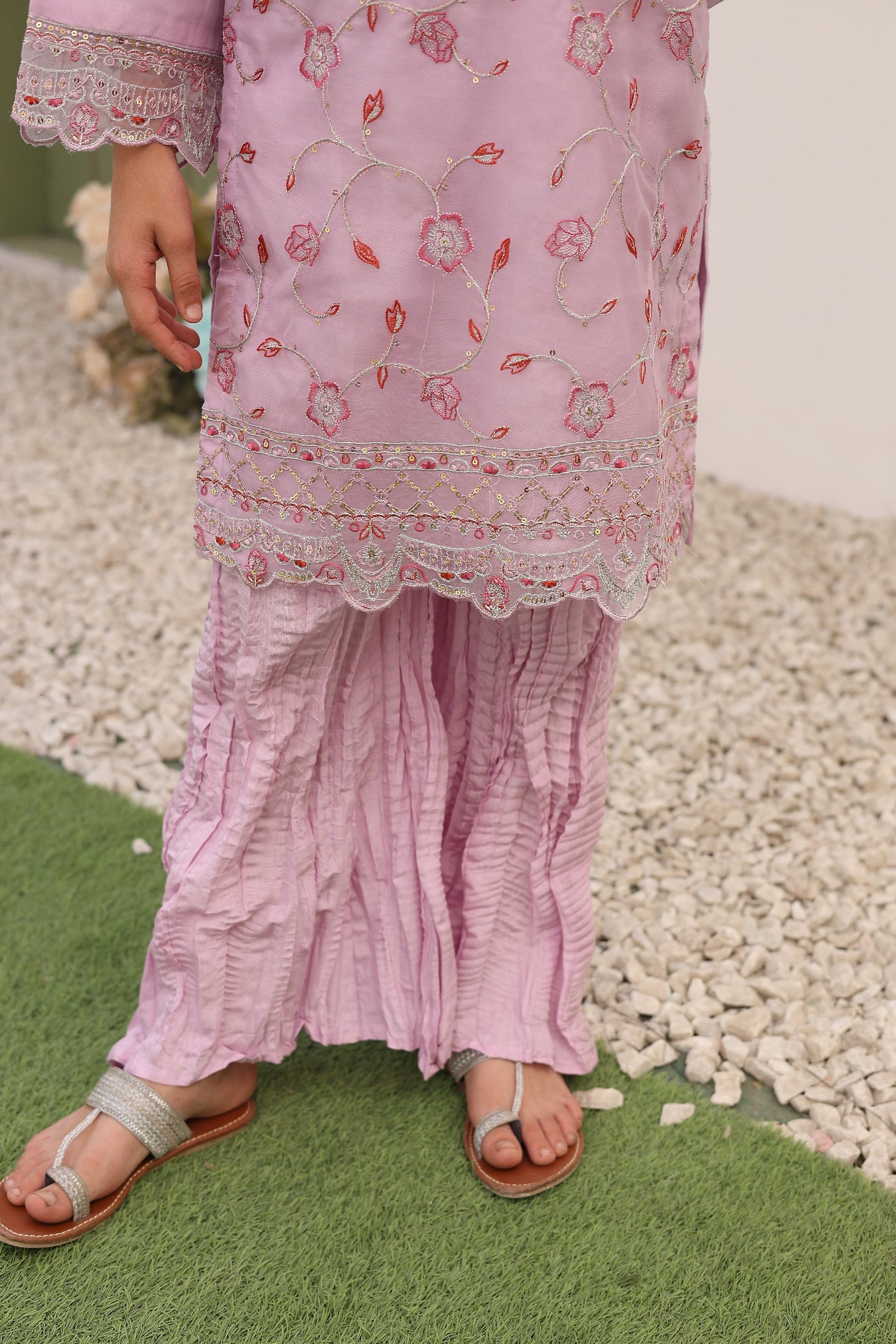 Person wearing a pink dress with floral embroidery on a grassy and stone surface.