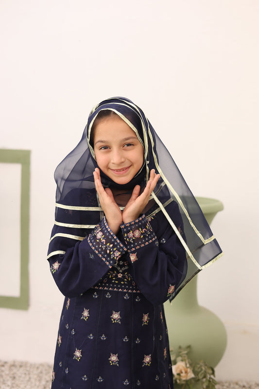 Woman wearing a navy blue hijab with white patterns, sitting on a light-colored floor.