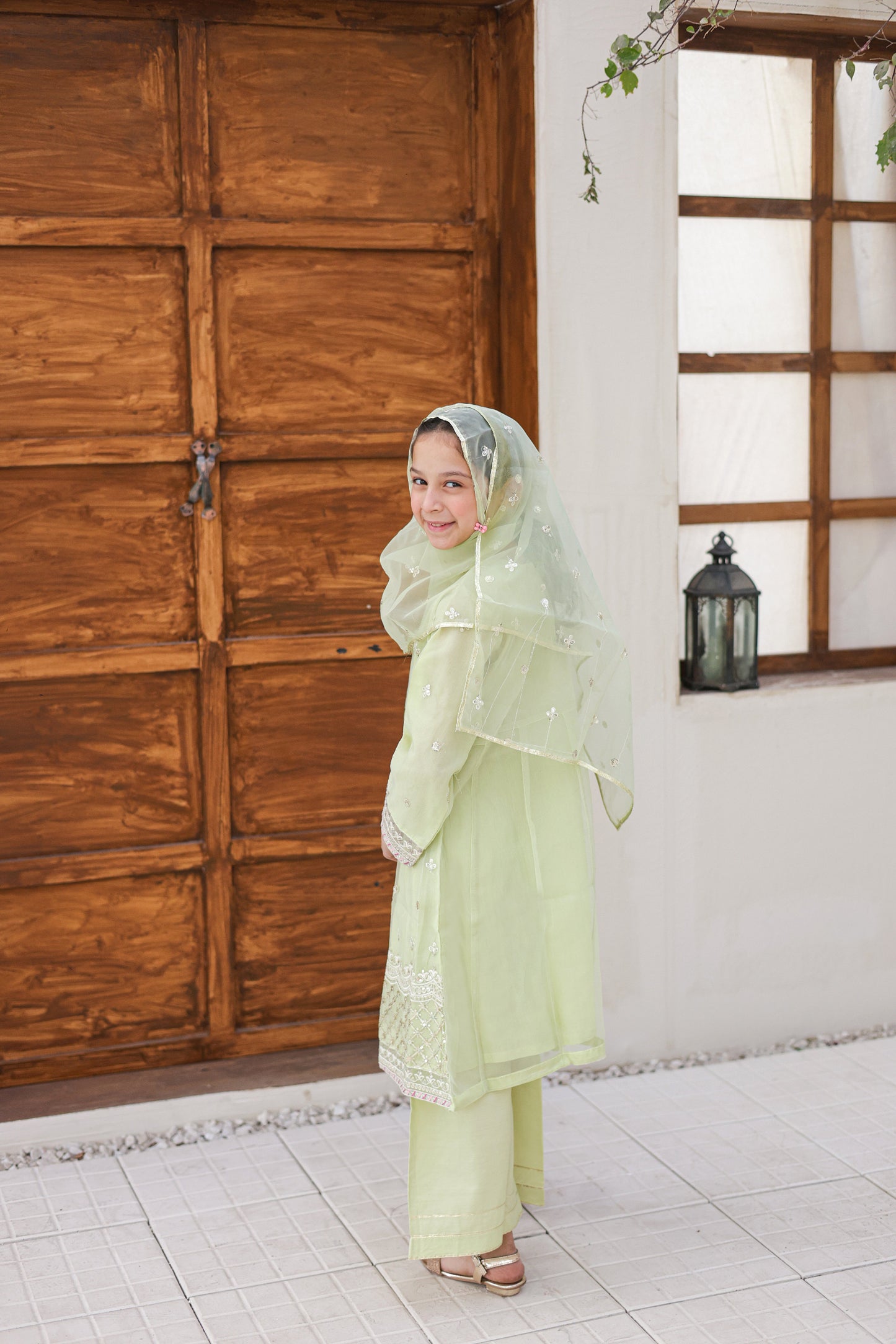 Woman in a light green traditional outfit standing in front of a wooden door.