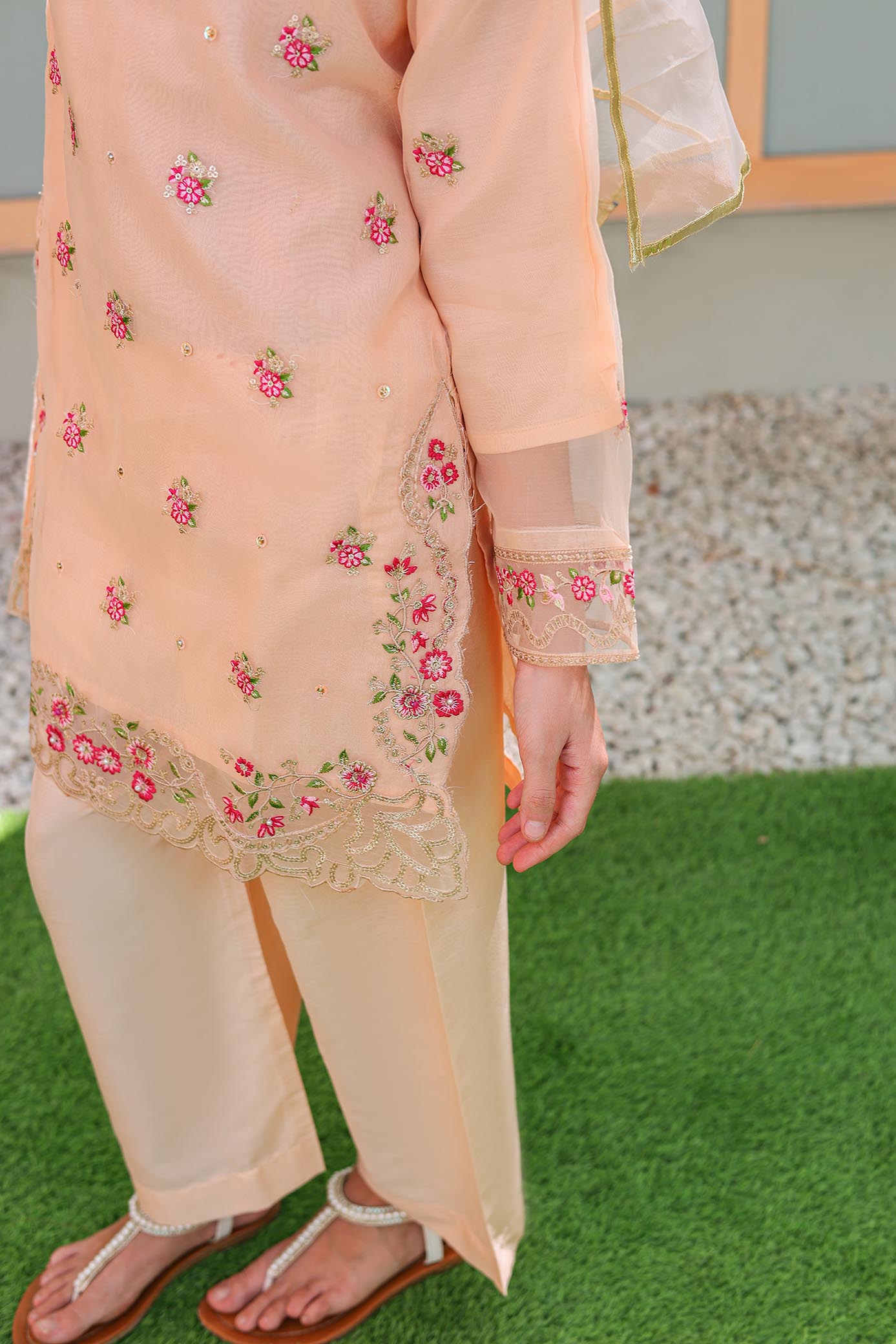 Person wearing a peach embroidered outfit on a grassy surface