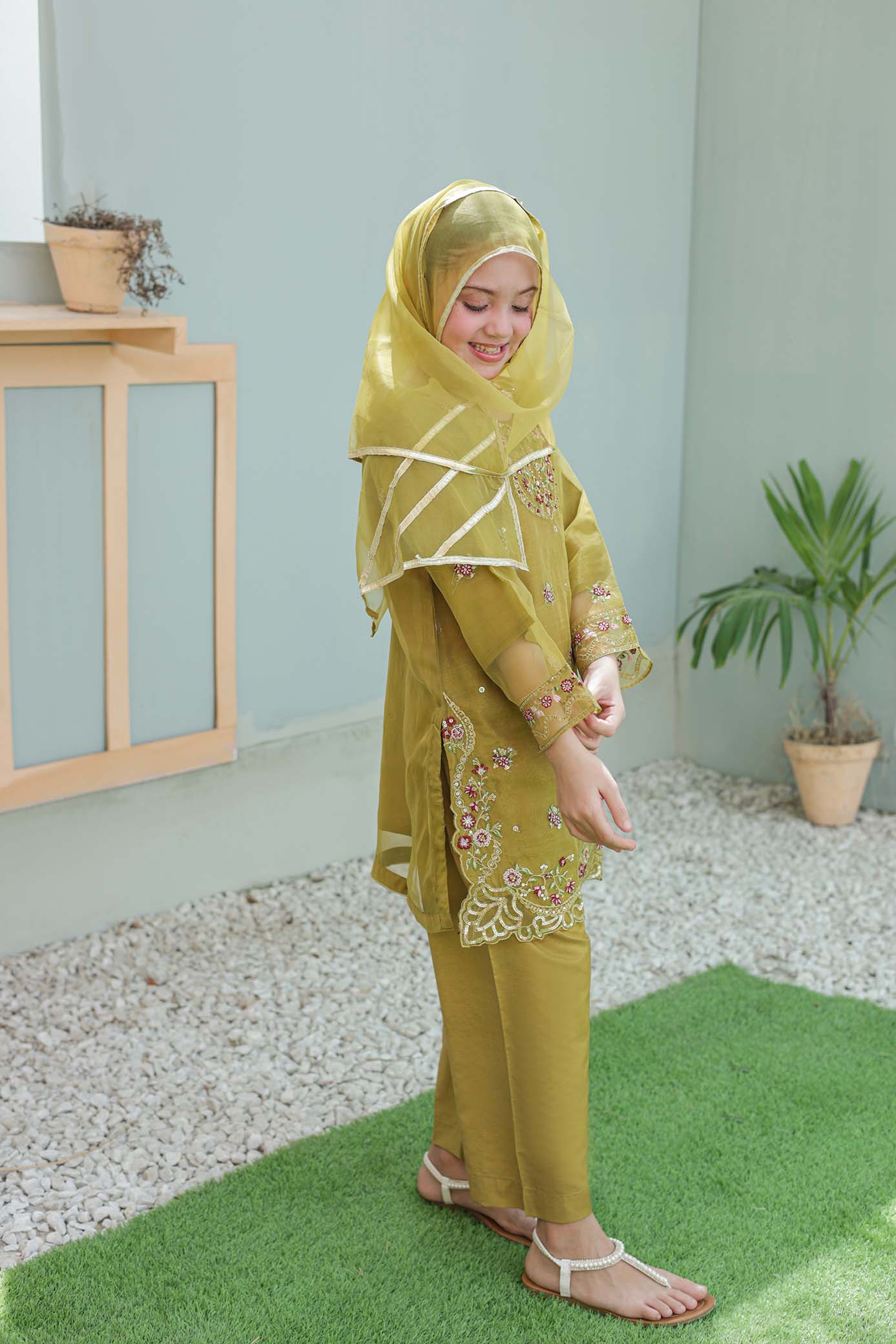 Woman wearing a green traditional outfit with a matching hijab in an indoor setting.
