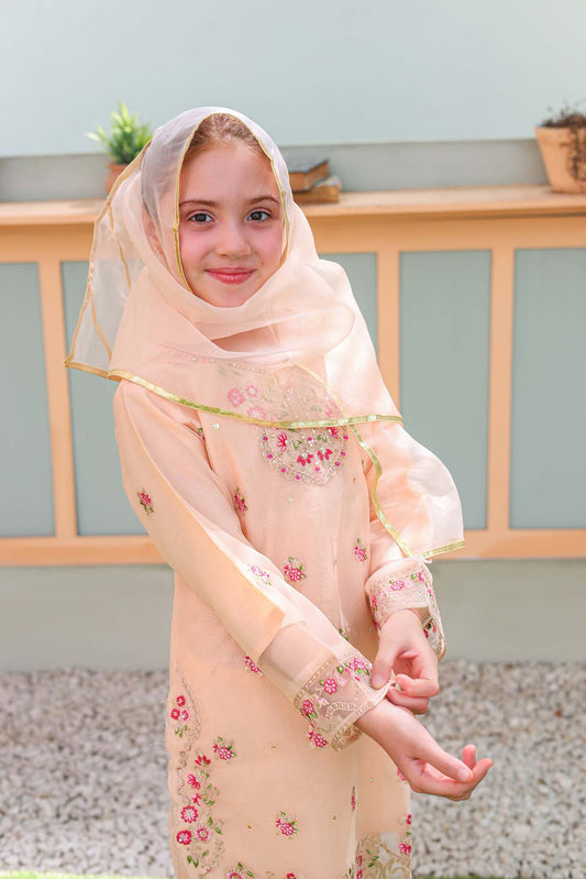 Young girl wearing a light pink floral dress and headscarf outdoors.