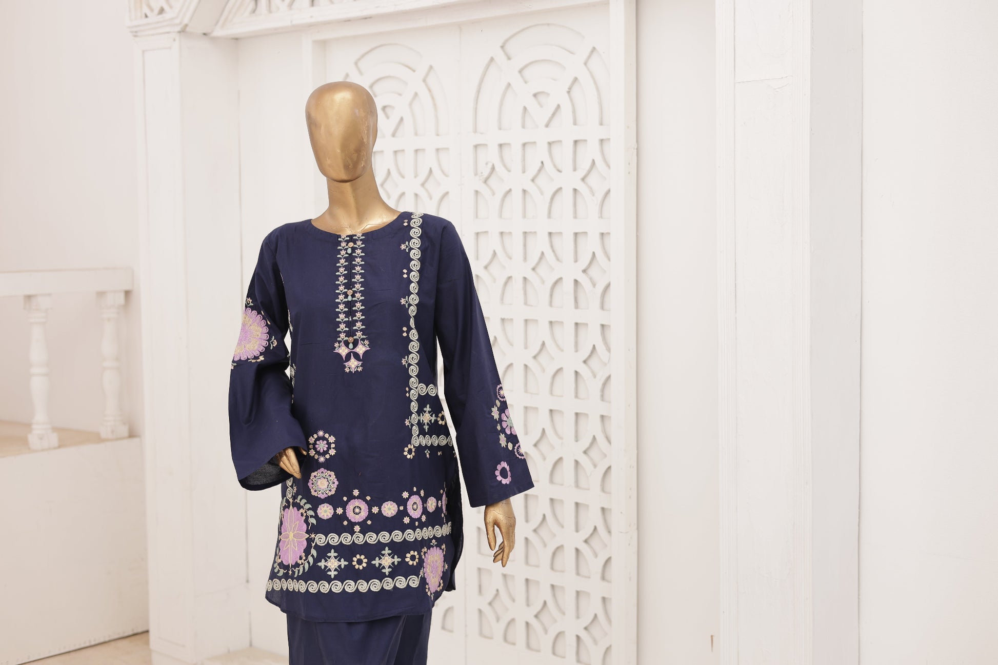 Navy blue embroidered outfit on a mannequin against a white decorative wall.