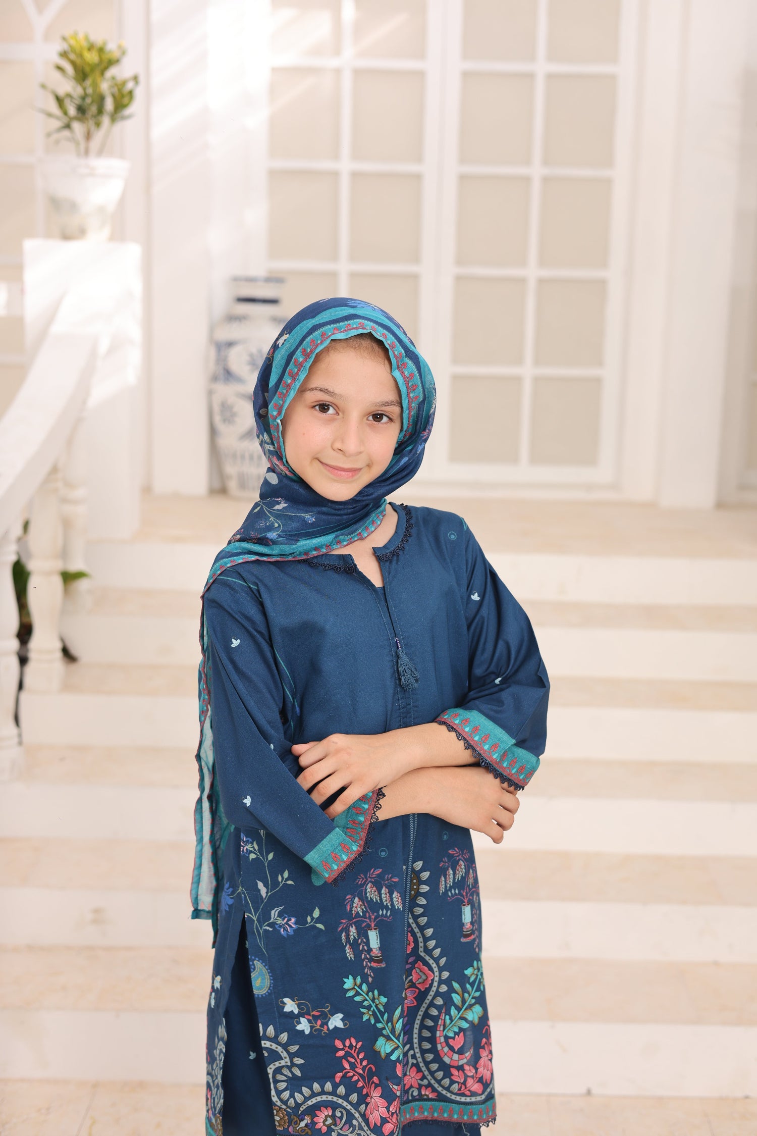 Young girl wearing a blue traditional outfit with a matching headscarf indoors.