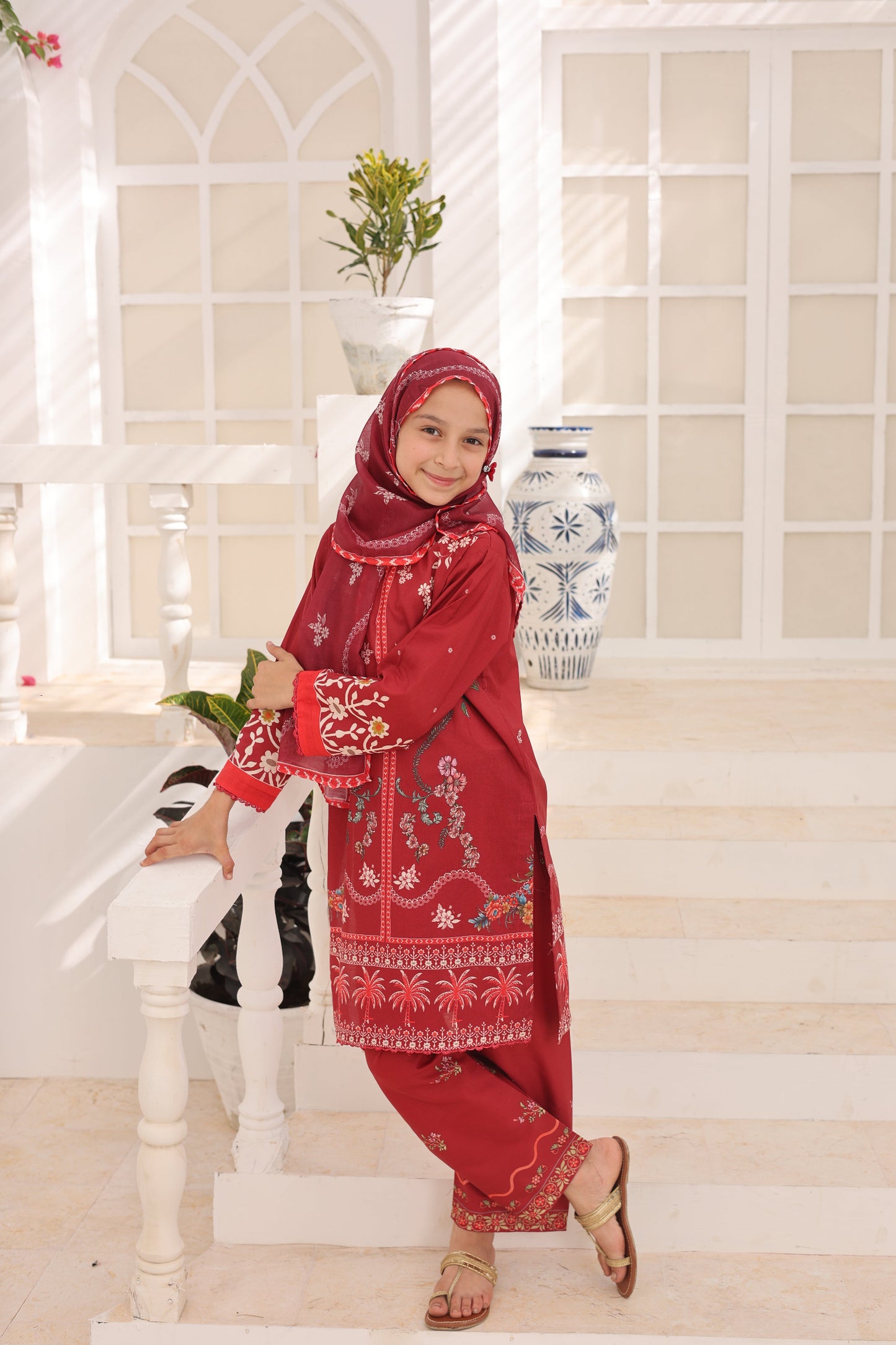 Child wearing a red traditional outfit with embroidery in a bright room.