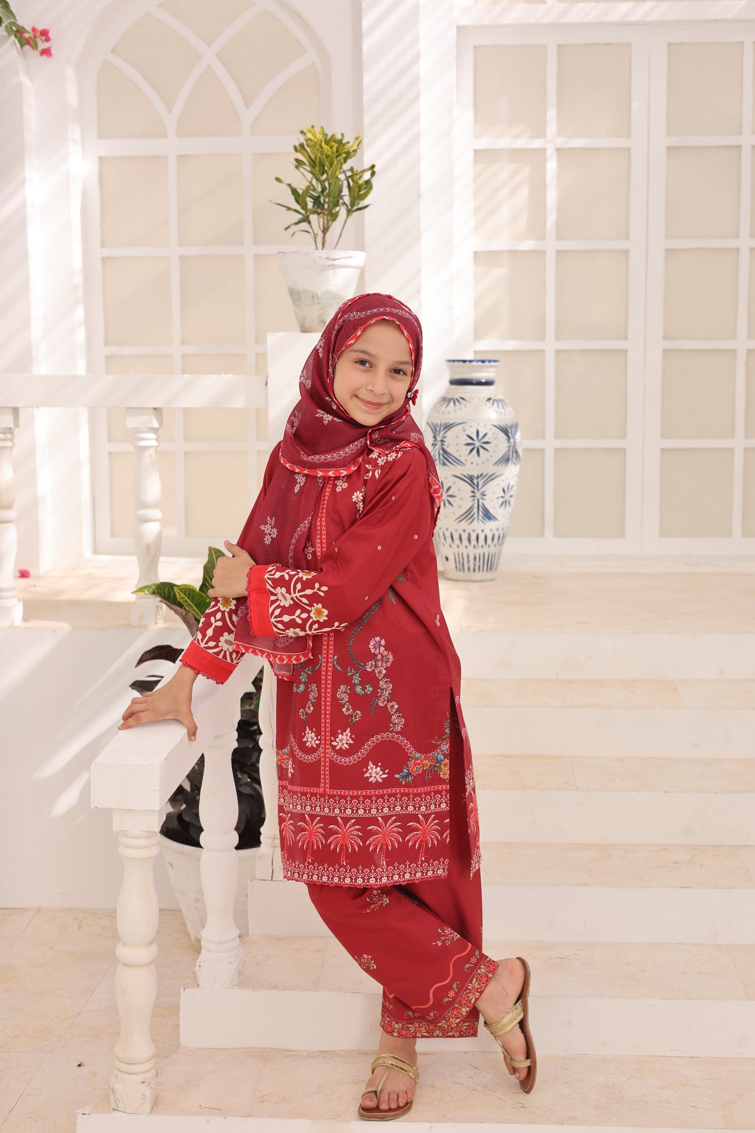 Child wearing a red traditional outfit with embroidery in a bright room.