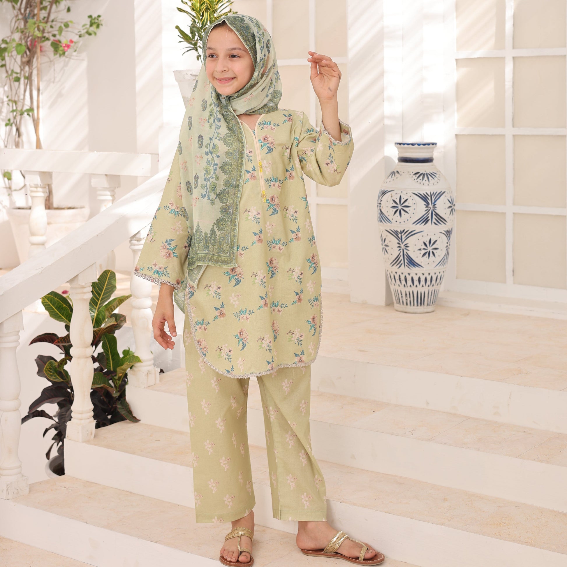Woman in a light green outfit with floral patterns standing on a white floor with decorative plants.