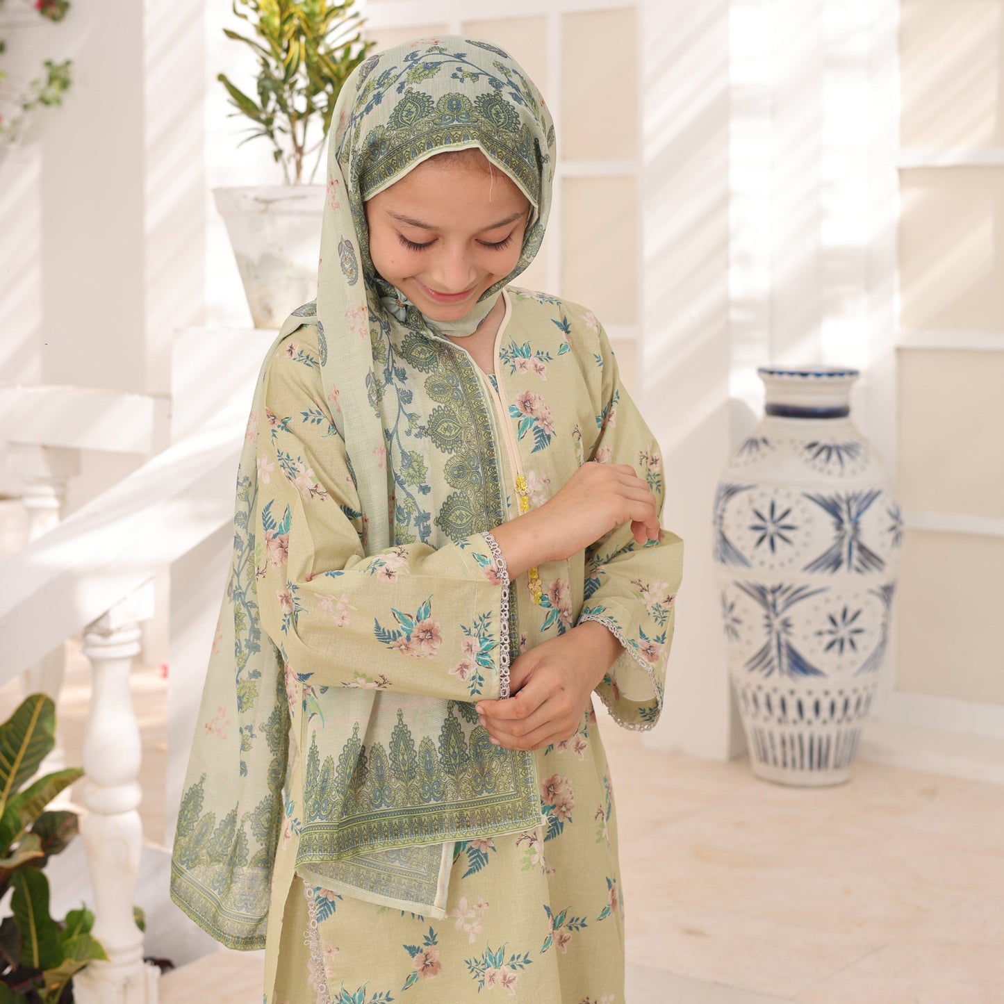 Woman in a floral dress and headscarf holding a bottle with a white background