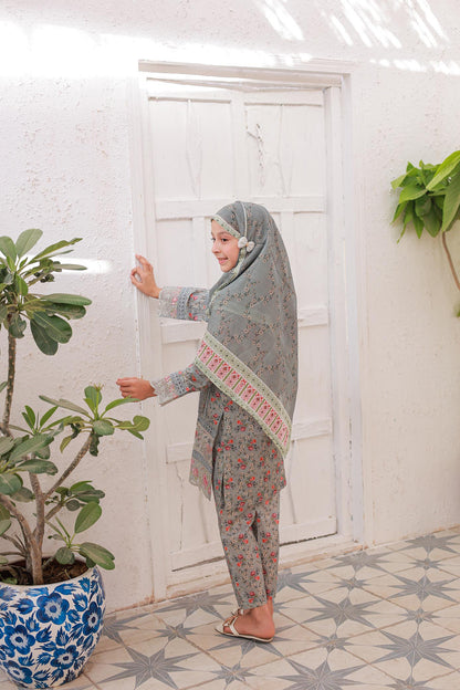 Woman in a patterned outfit standing in a room with plants and a white door.