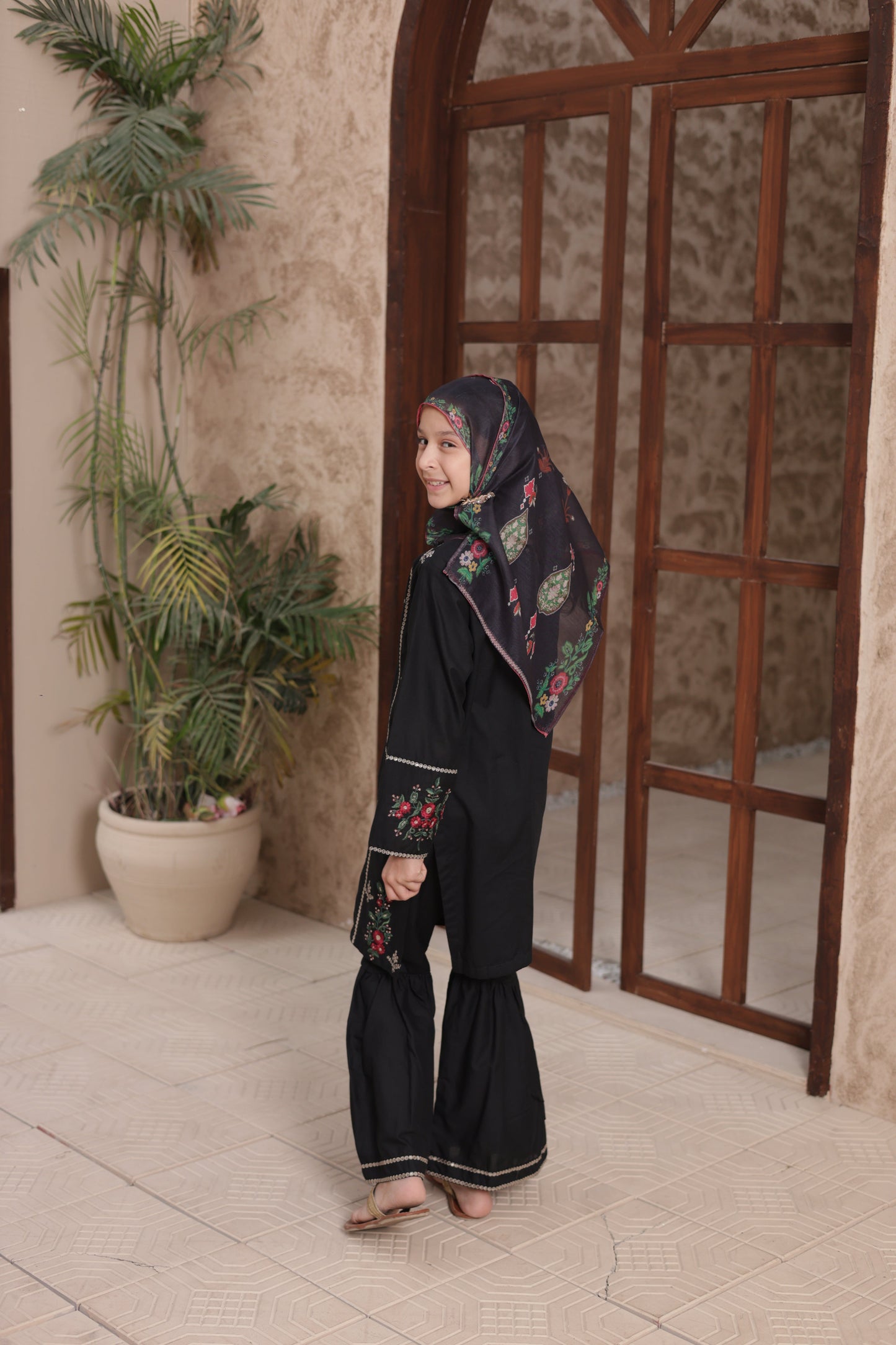 Person wearing a floral headscarf and dark clothing standing on a wooden staircase.