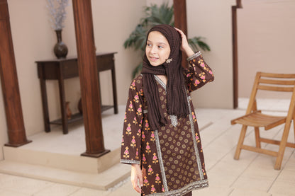 Young girl wearing a patterned dress and hijab indoors.