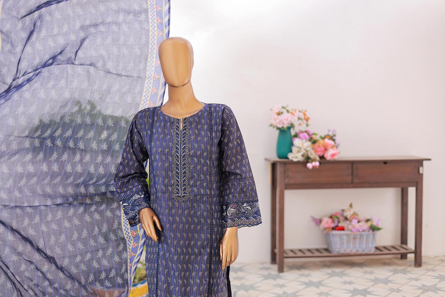Mannequin wearing a blue patterned dress with a large fabric swatch and flowers in the background.