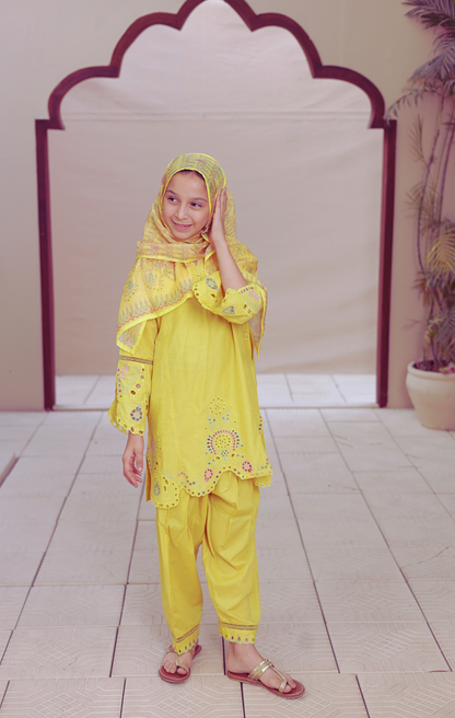 Child wearing a yellow traditional outfit with a headscarf in a decorative setting.