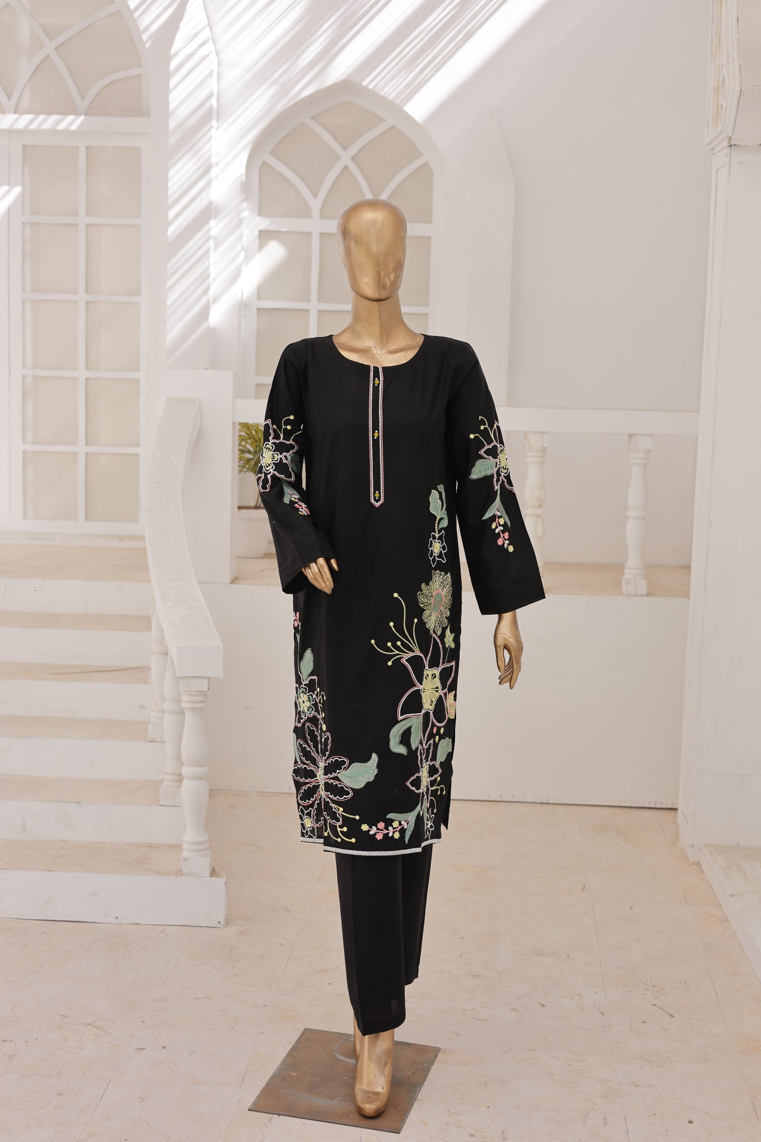 Black embroidered outfit on a mannequin in a bright room with white walls and a staircase.