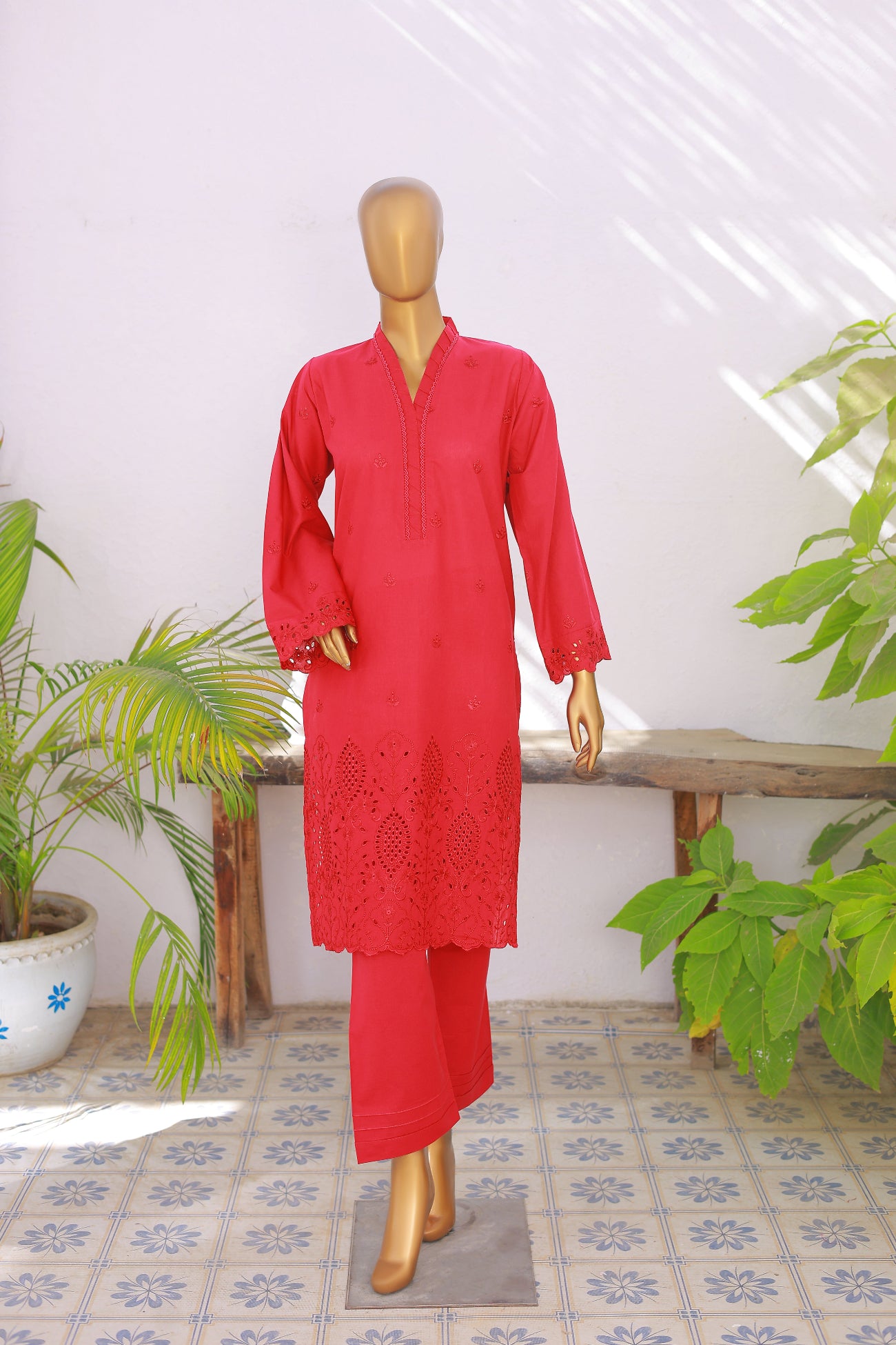 Red kurta with lace detailing on a mannequin against a white wall with plants.