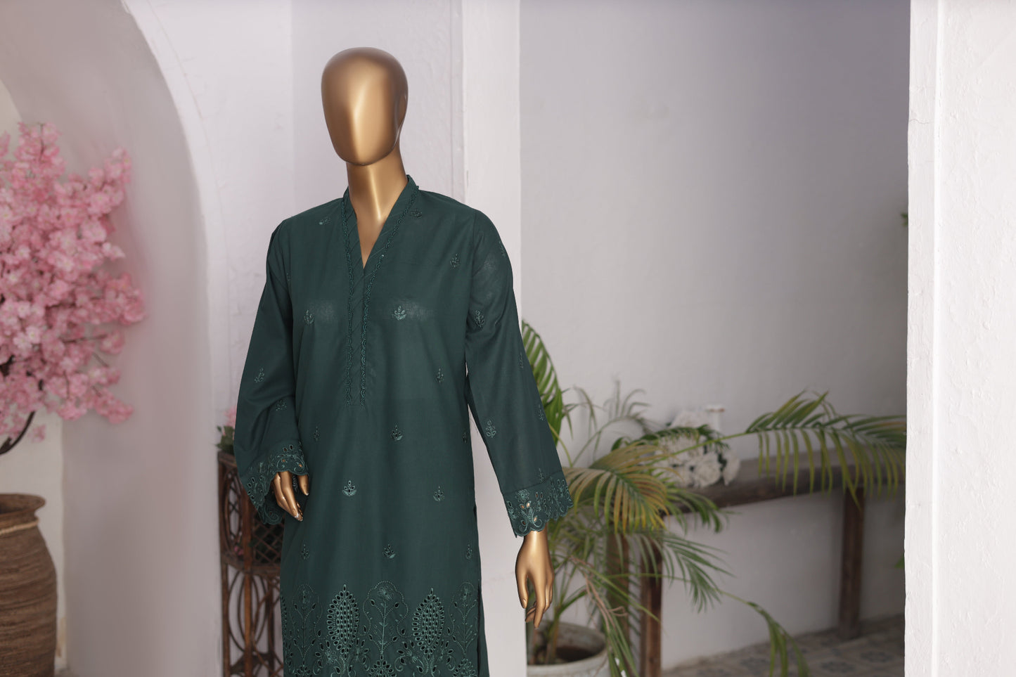 Mannequin wearing a dark green traditional outfit with floral patterns in an indoor setting.