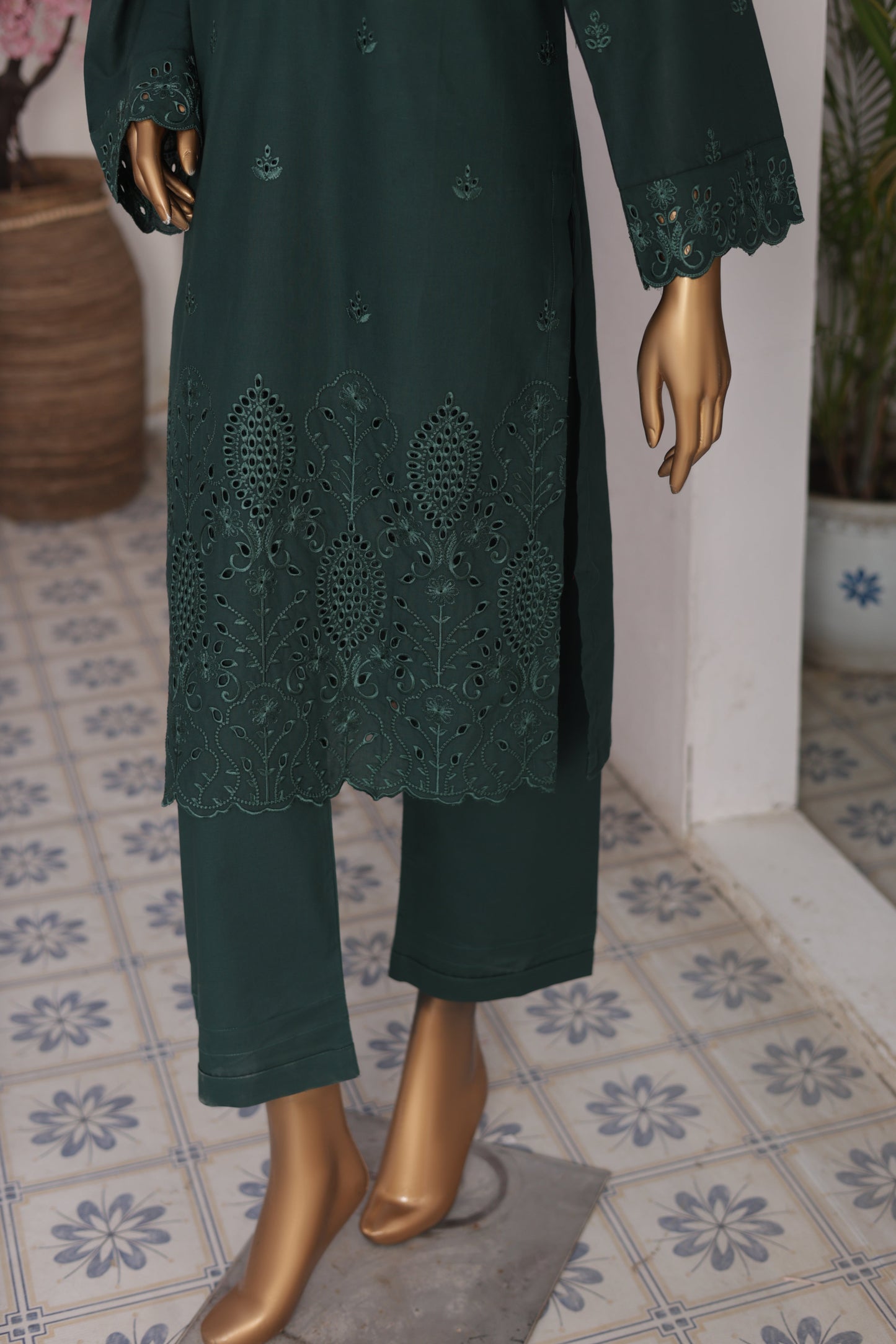 Dark green embroidered coat on a mannequin with gold shoes against a tiled floor background