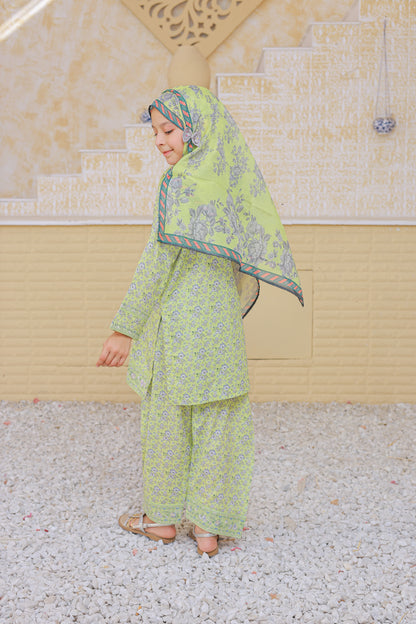 Woman in a green traditional outfit standing outdoors with a decorative wall in the background.