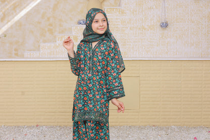 Child wearing a floral outfit with a headscarf standing against a beige wall.