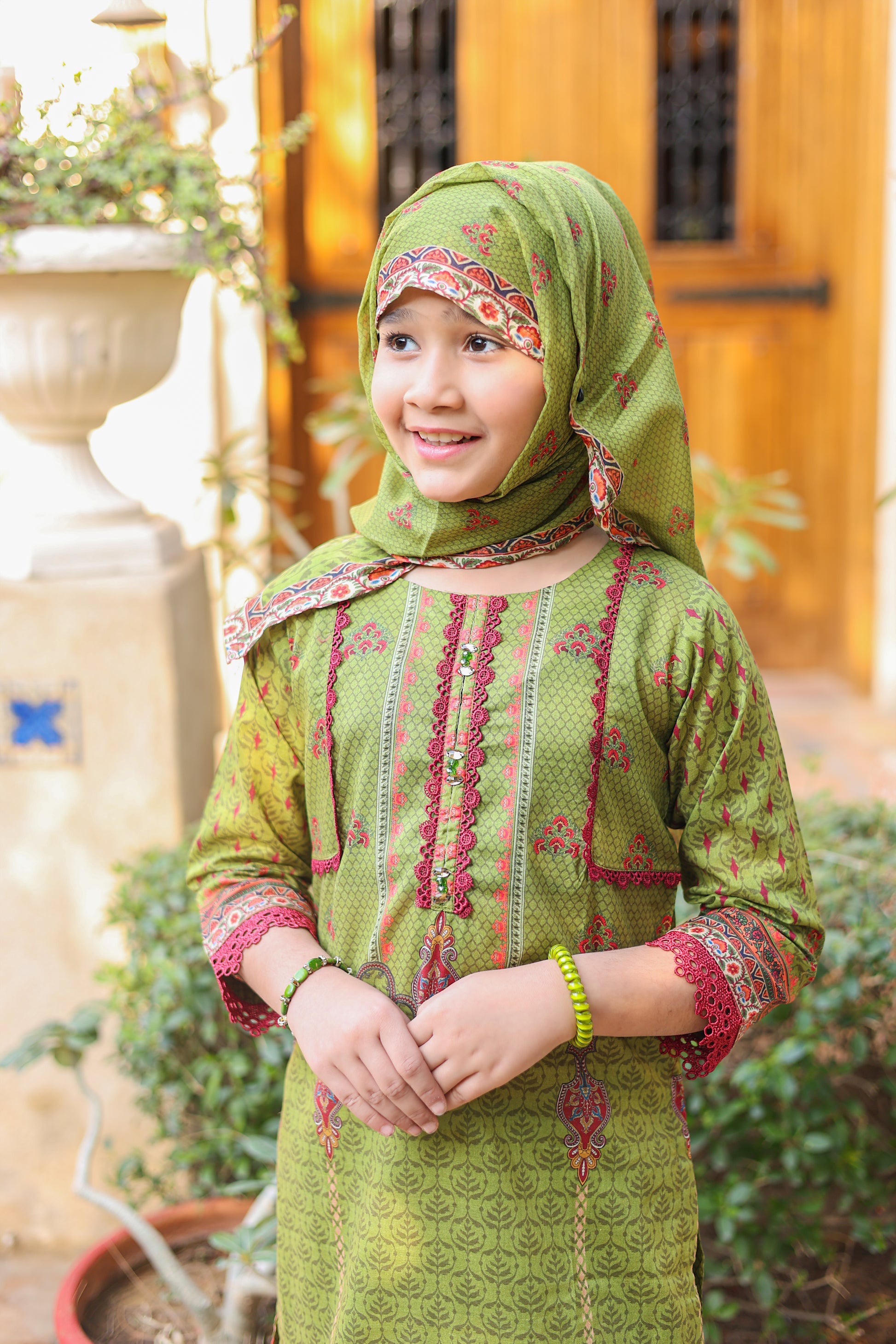 Young girl wearing a green traditional outfit with a matching headscarf in an outdoor setting.