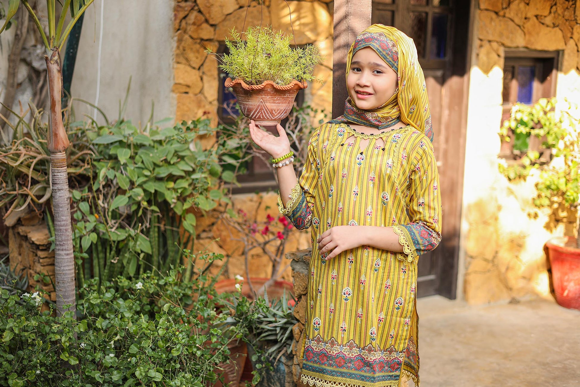 Woman in a yellow traditional outfit holding a plant in a garden setting