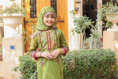 Young girl in a green traditional outfit standing outdoors with plants and a building in the background