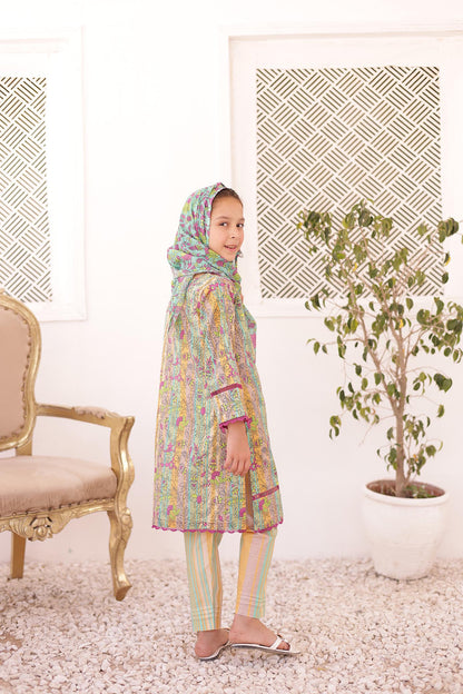 Child wearing a colorful traditional outfit in a room with a chair and plant.
