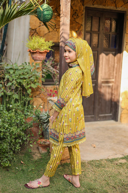 Child in a yellow traditional outfit standing outdoors with plants and a wooden door in the background