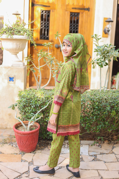 Woman in green traditional outfit standing outdoors with plants and a wooden door in the background