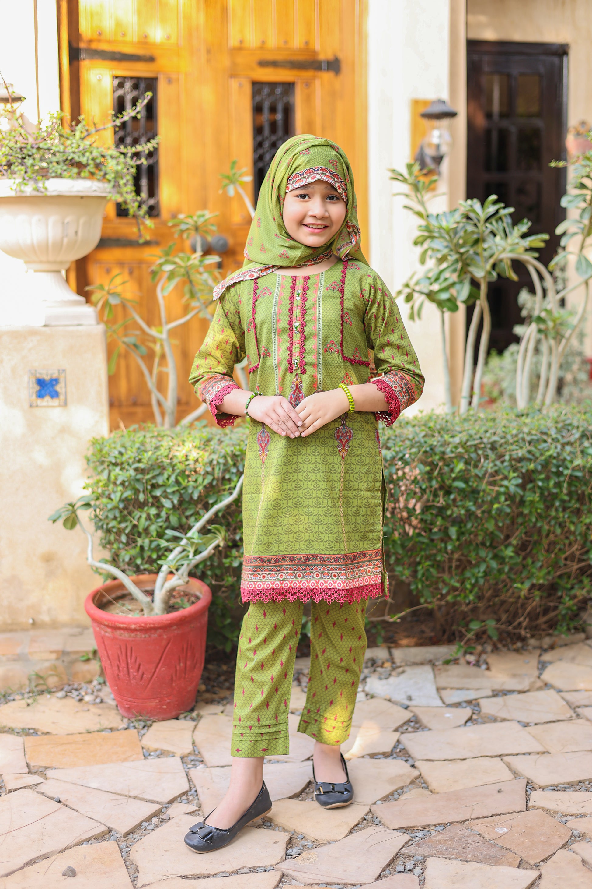 Child wearing a green traditional outfit with a hood in an outdoor setting.