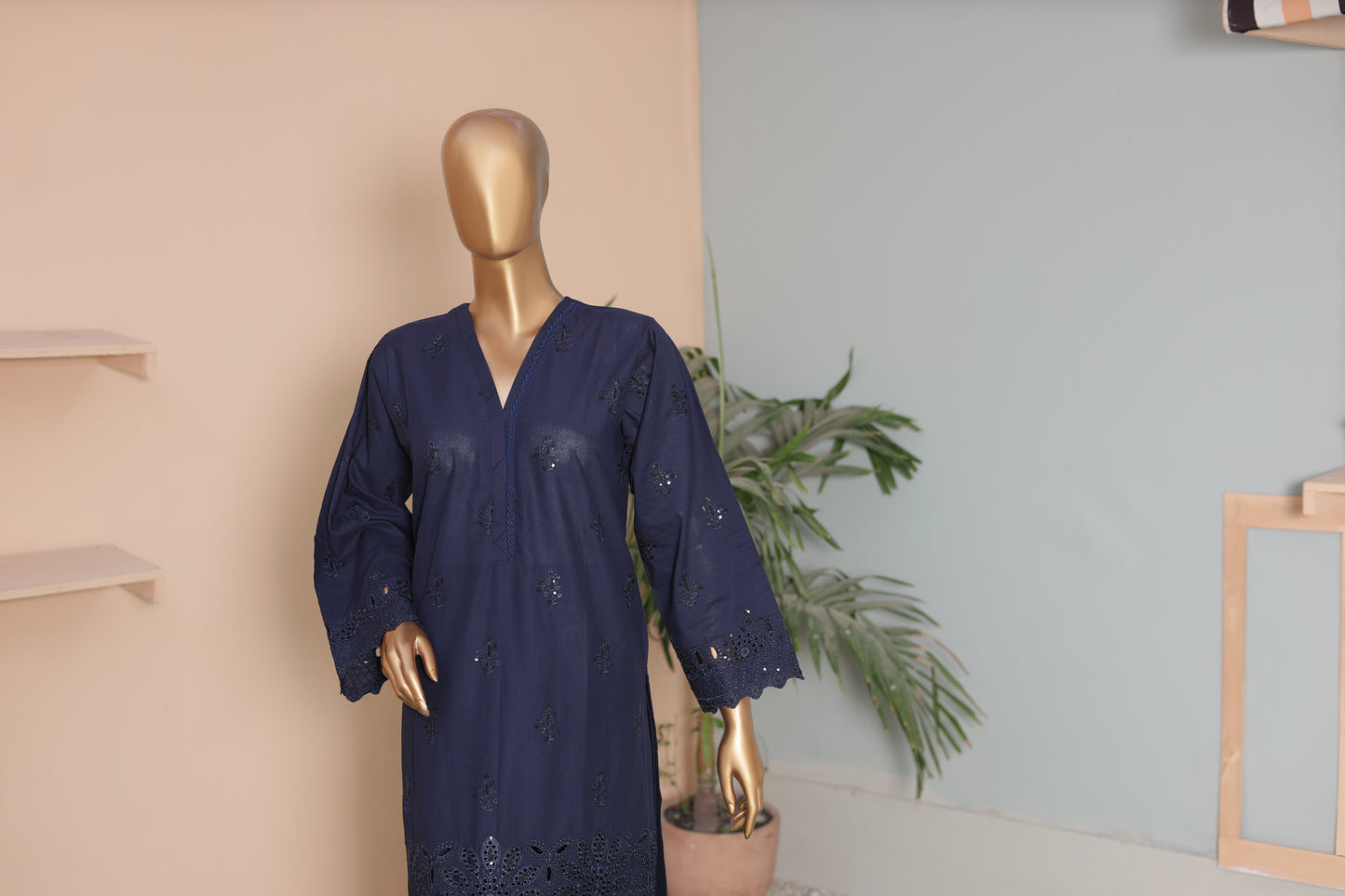 Navy blue dress on a mannequin against a neutral wall with a plant in the background