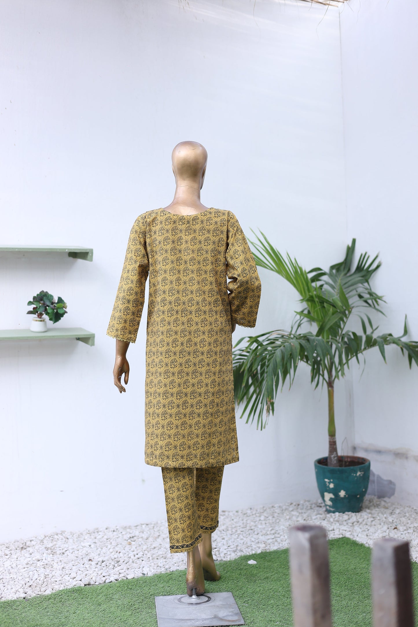 Mannequin wearing a patterned dress with a white background and plants.