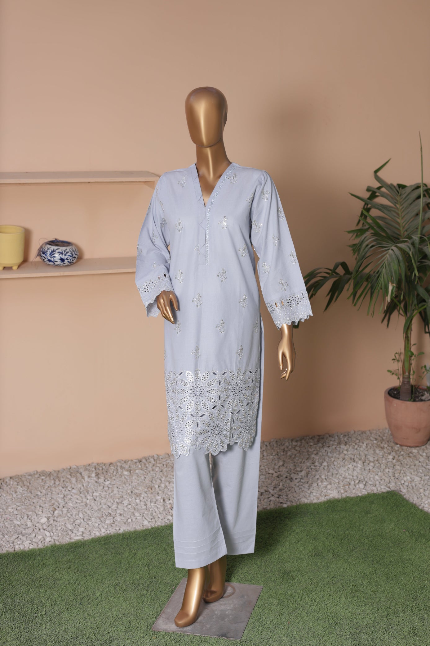 Mannequin wearing a light blue outfit with lace details in a room with a beige wall and green rug.